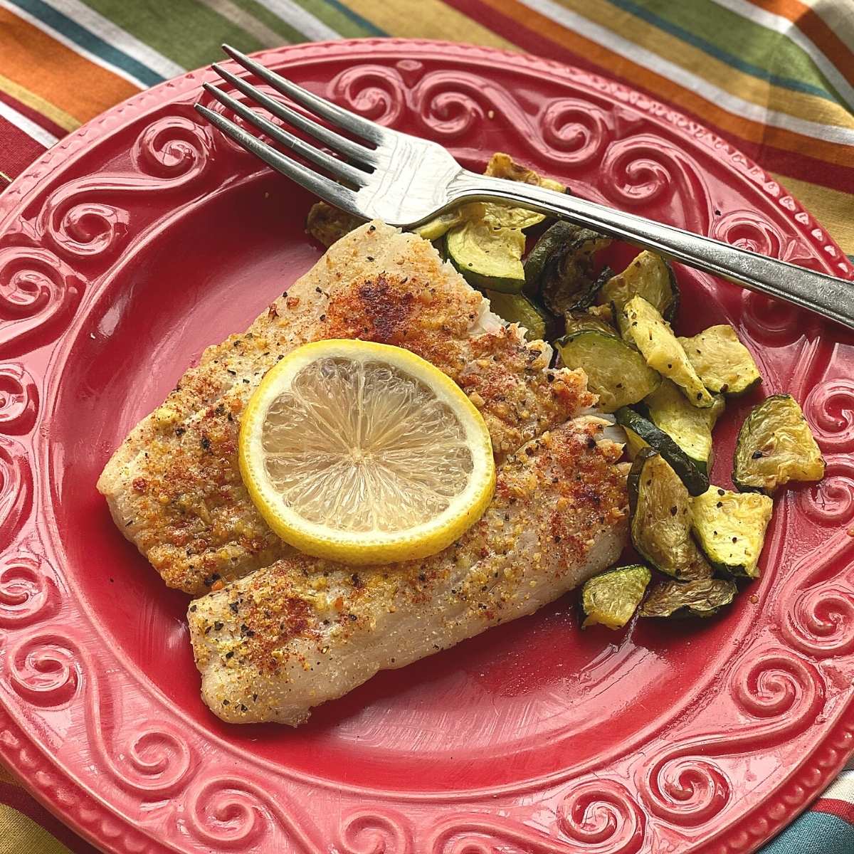 Baked corvina and zucchini on a plate with a fork.