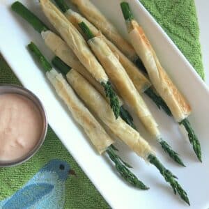 Phyllo wrapped asparagus on a platter next to aioli in a cup.
