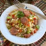 Cajun cauliflower rice with andouille sausage in a bowl with a fork resting on the edge.