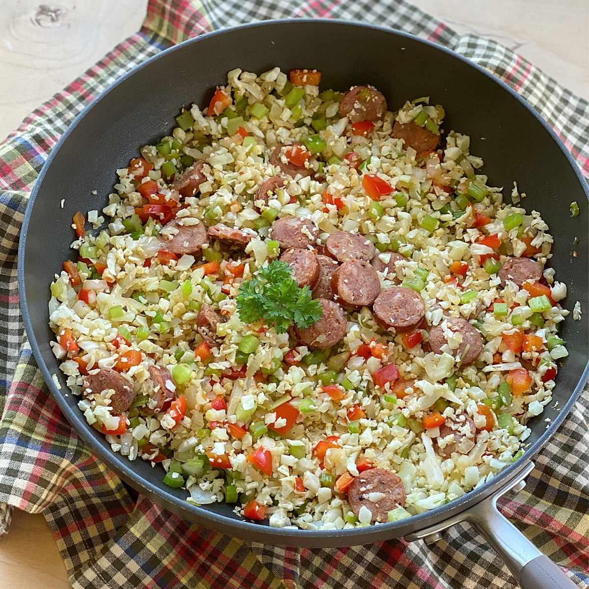 Skillet with Cajun cauliflower rice topped with sausage and garnished with parsley.