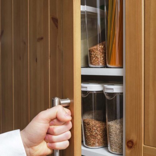 Hand opening the door of an organized pantry with decanted storage containers inside.