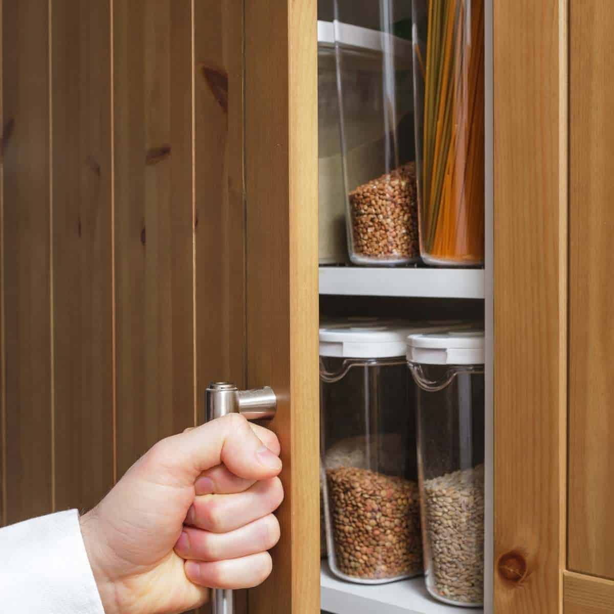 Hand opening the door of an organized pantry with decanted storage containers inside.