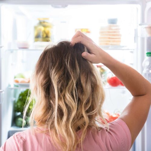 Person scratching that back of head looking into an organized refrigerator with the doors open.