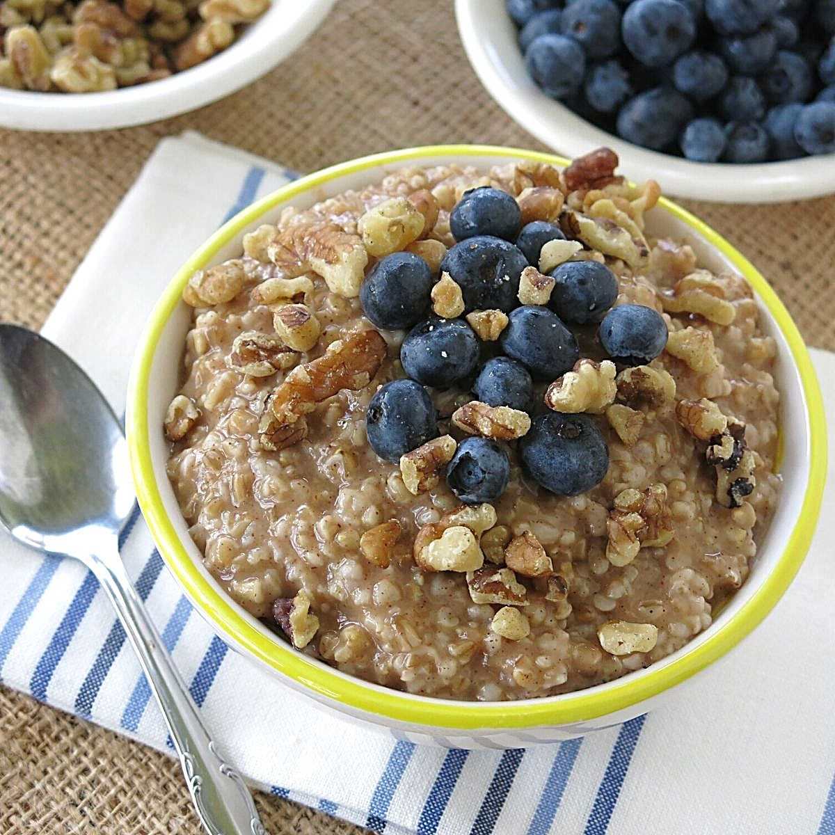 Bowl of slow cooker steel cut oatmeal with blueberries and walnuts on top and more blueberries in the background.