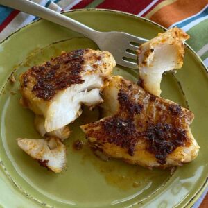 Blackened cod fish fillet on a plate with fork holding a bite to see white flaky flesh.