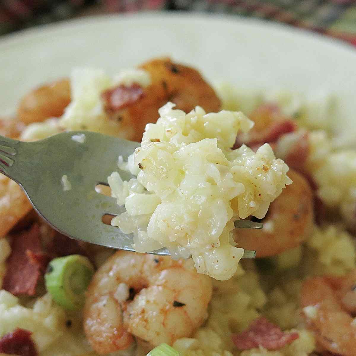 Fork holding a bite of grits that are creamy from the cheese.