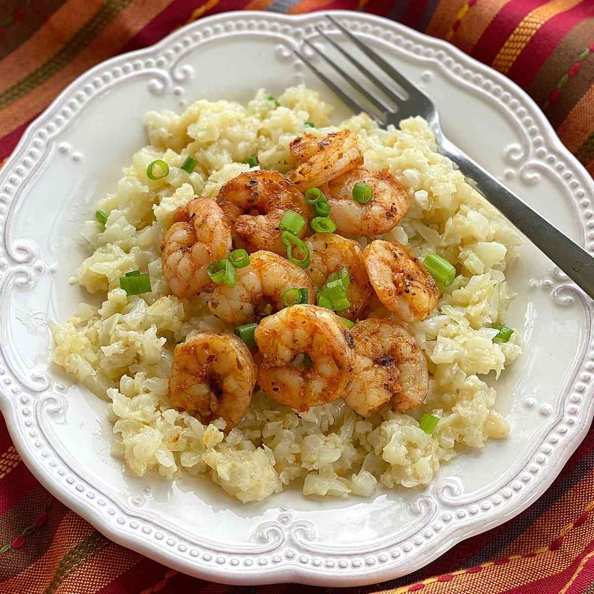 Cheesy cauliflower grits and spicy shrimp on a plate topped with a fork.