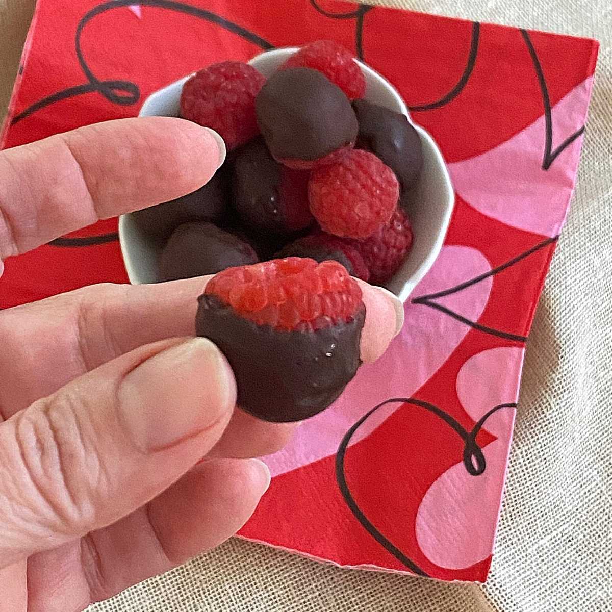 Hand holding one dark chocolate dipped raspberry.