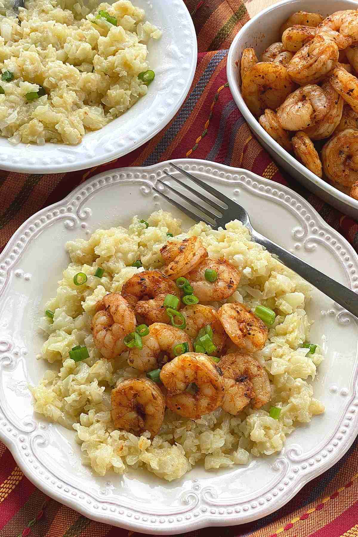 Plate with a serving of recipe with bowl of cauliflower grits and shirmp in the background.