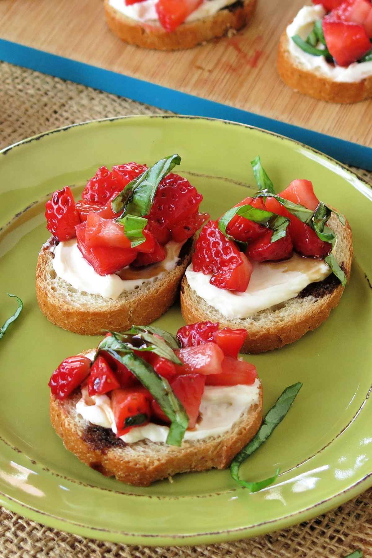 Plate with 3 slices of strawberry bruschetta cream cheese appetizer topped with basil and balsamic vinegar glaze.