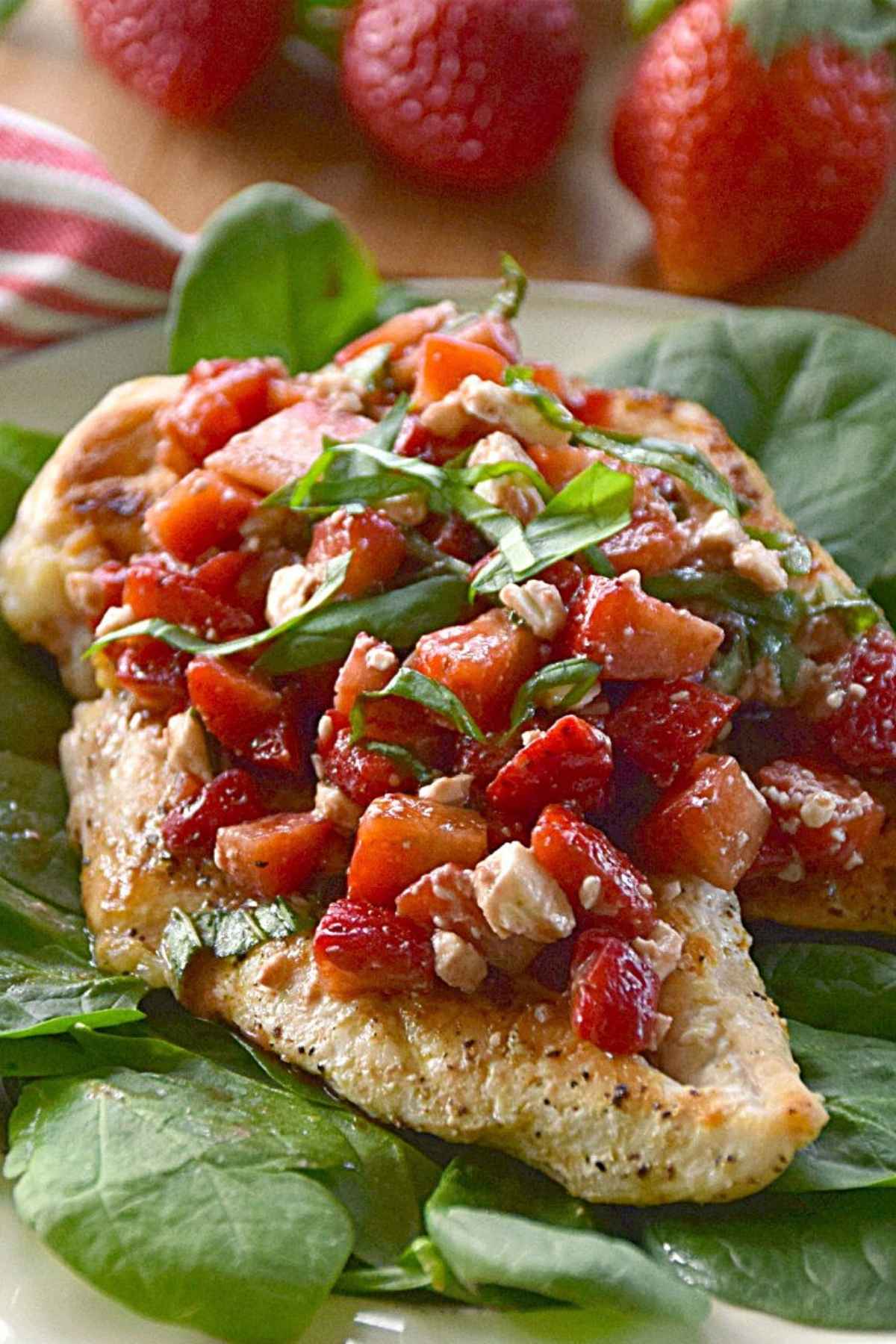 Strawberry chicken with a strawberry, fresh basil, and balsamic glaze topping on a bed of spinach leaves.