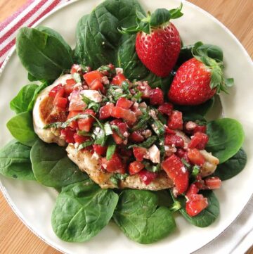 trawberry Chicken with an elegant bruschetta topping with basil and balsamic vinegar on a plate with spinach leaves and more strawberries in the background.