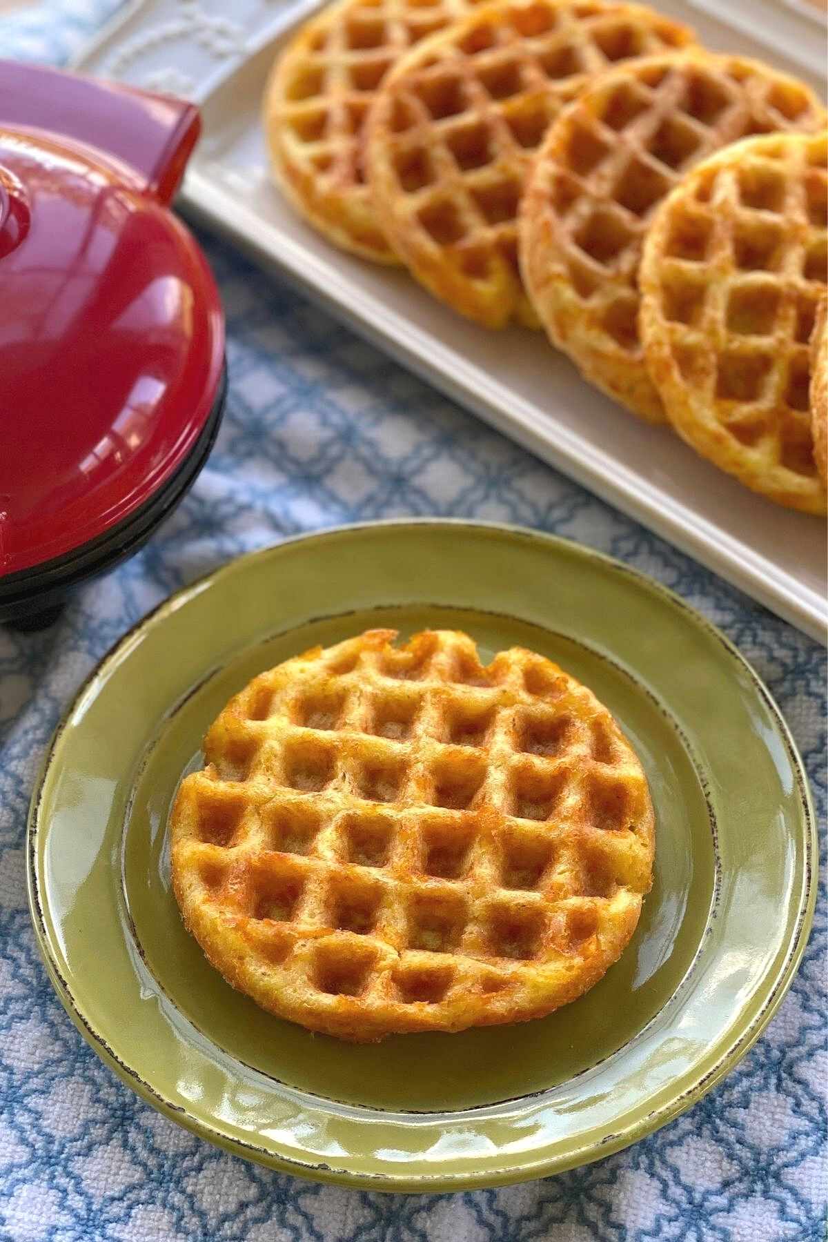 Basic keto chaffle on plate with more on platter behind it.