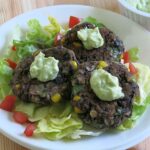 3 black bean cakes on a plate topped with avocado cream