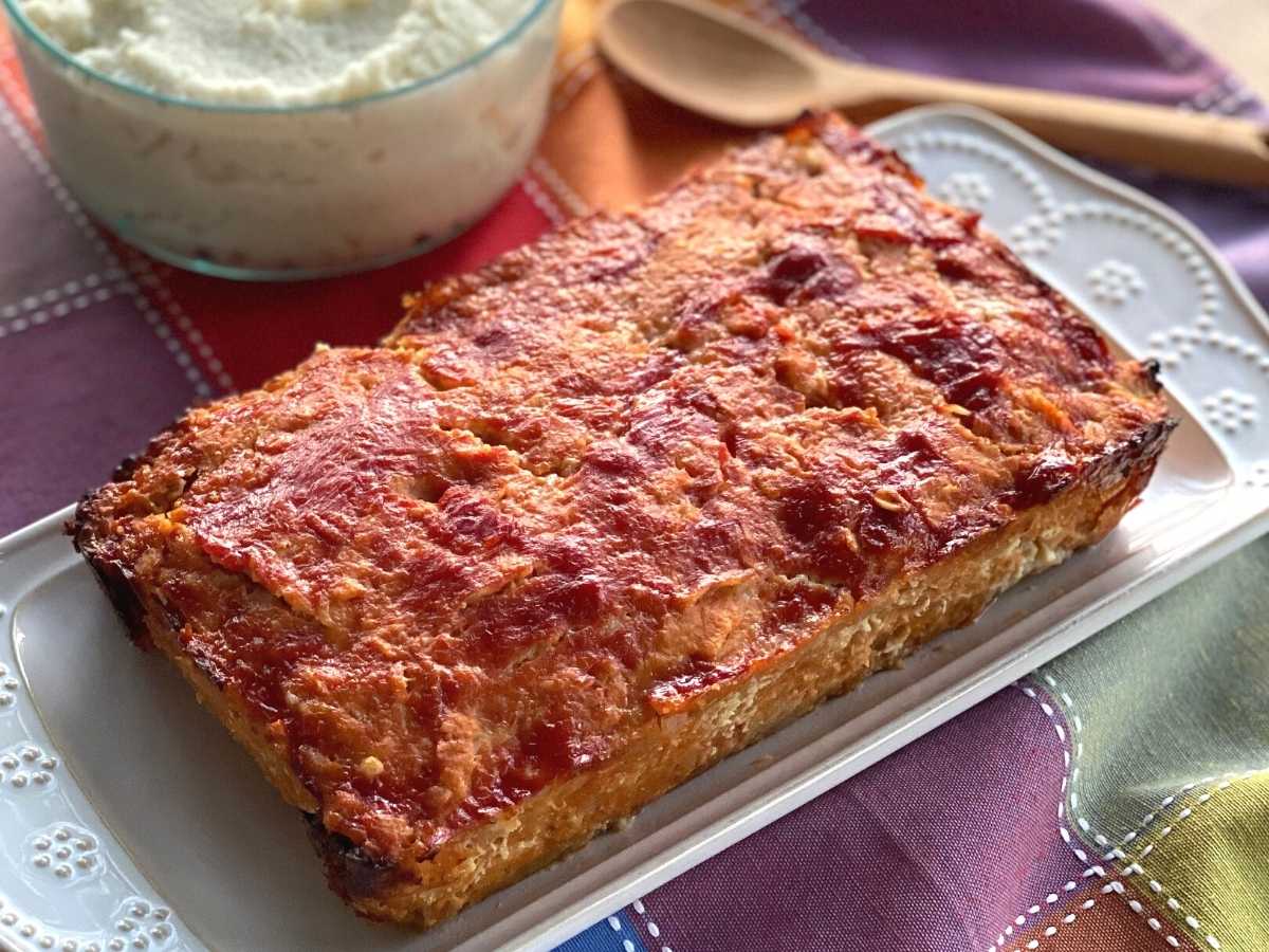 Chicken meatloaf on platter with bowl of mashed potatoes behind it.