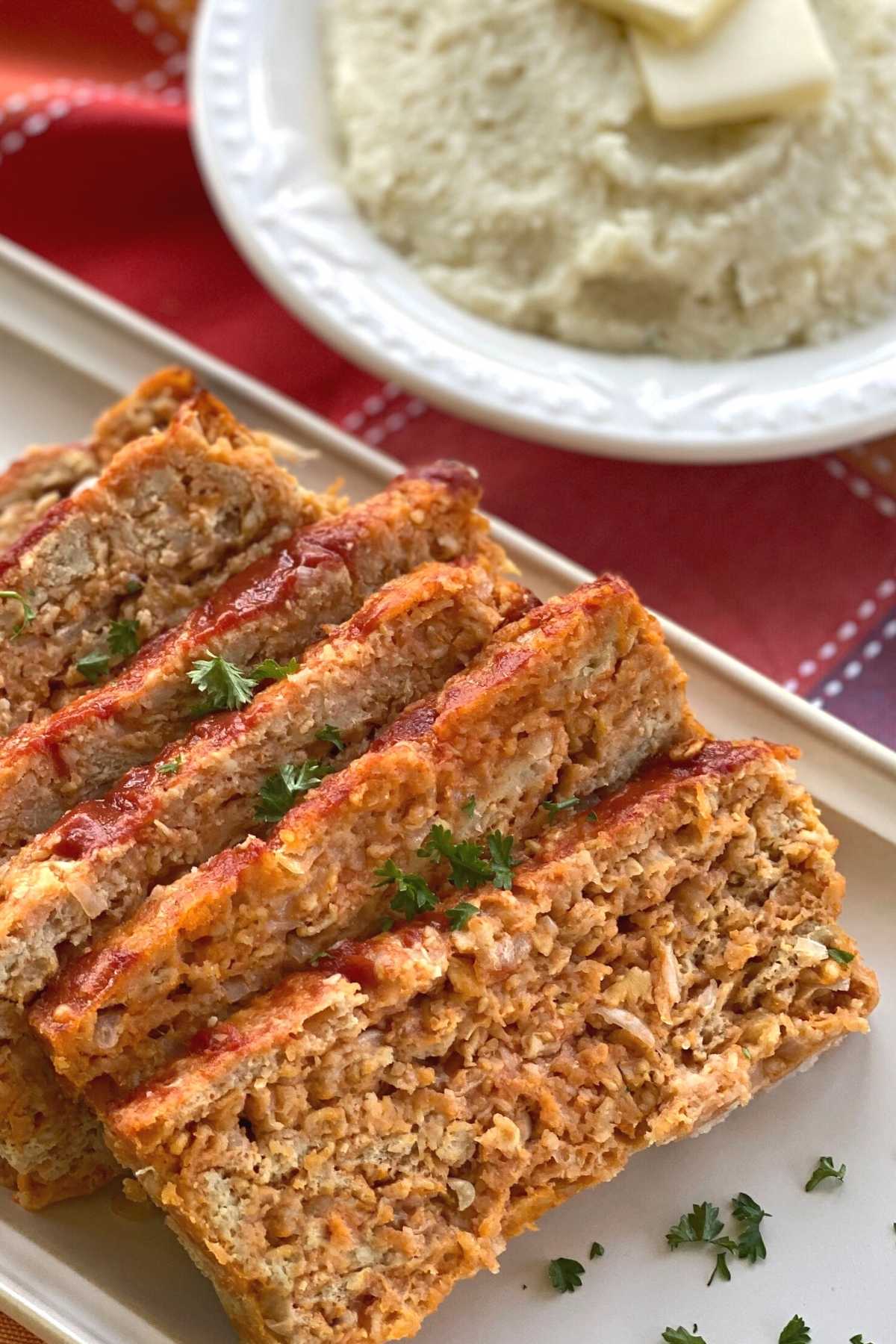 Slices of chicken meatloaf on a platter next to a bowl of cauliflower mash.