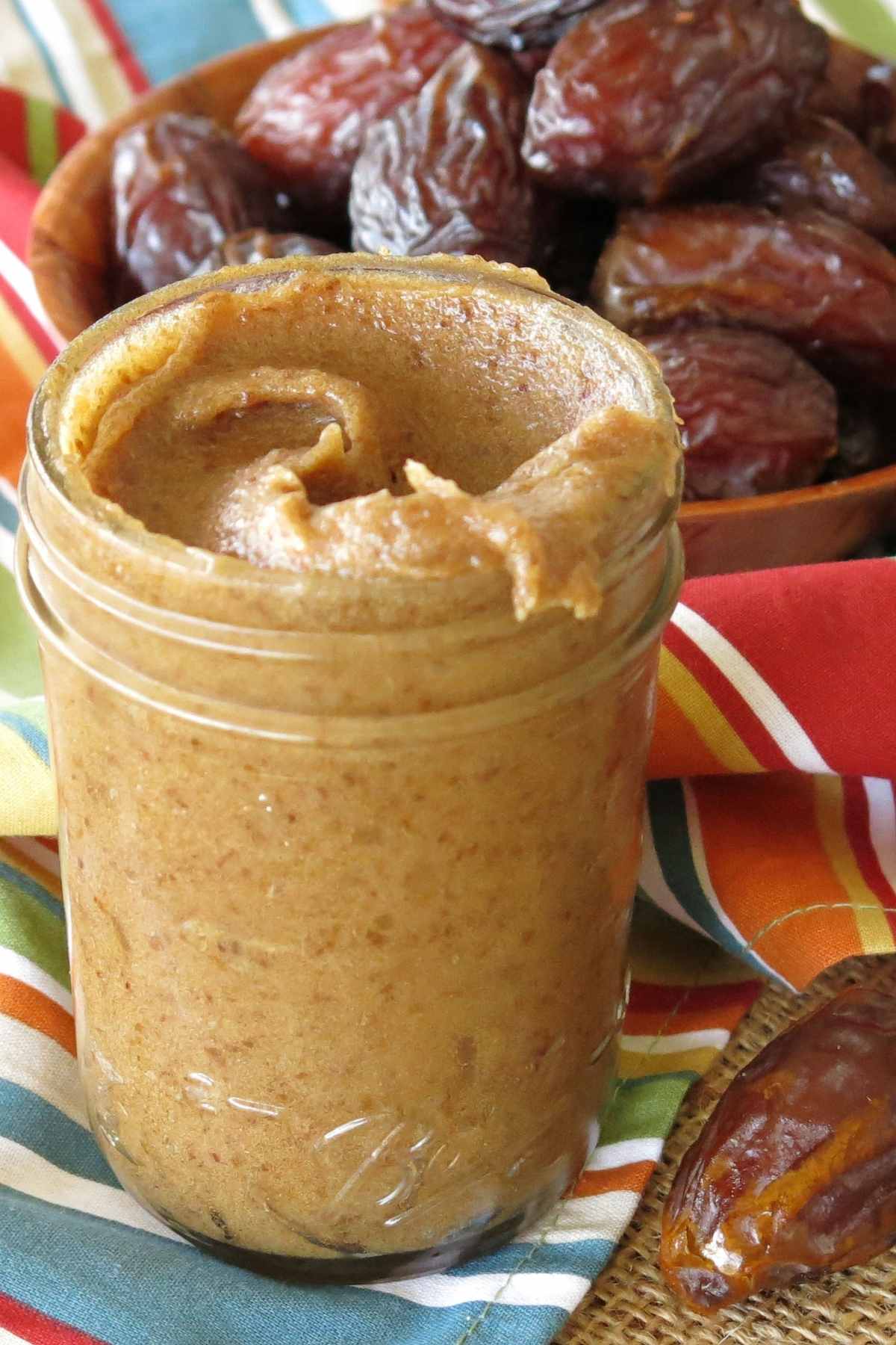 Jar of date jam spread with Medjool dates in the background.