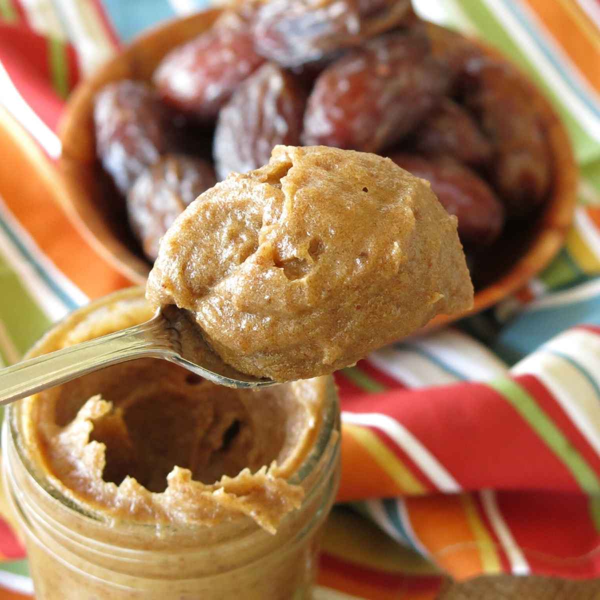 Date jam on a spoon over an open mason jar with the spread and Medjool dates in the background.