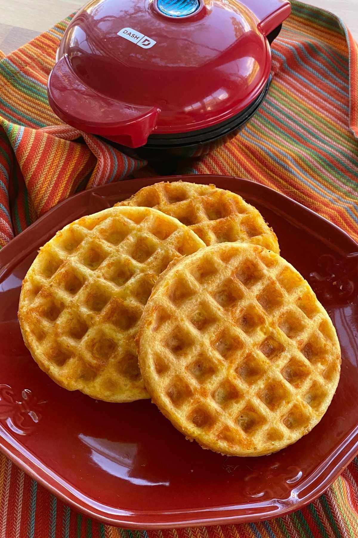 Easy keto chaffles on a plate with a dash mini waffle maker behind it.