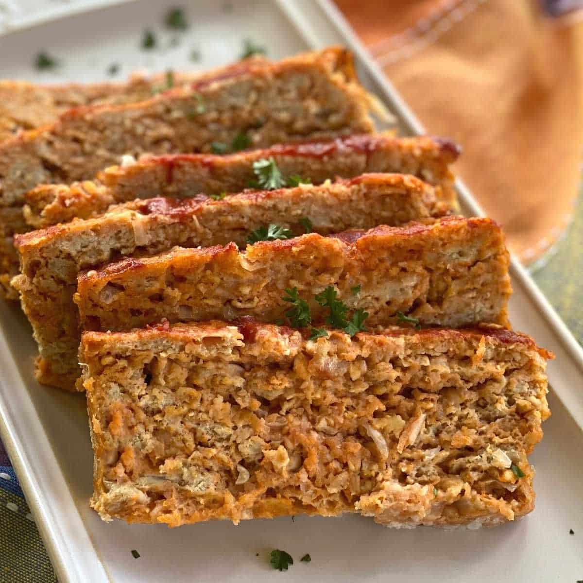 Slices of chicken meatloaf on a platter with parsley garnish over the top.