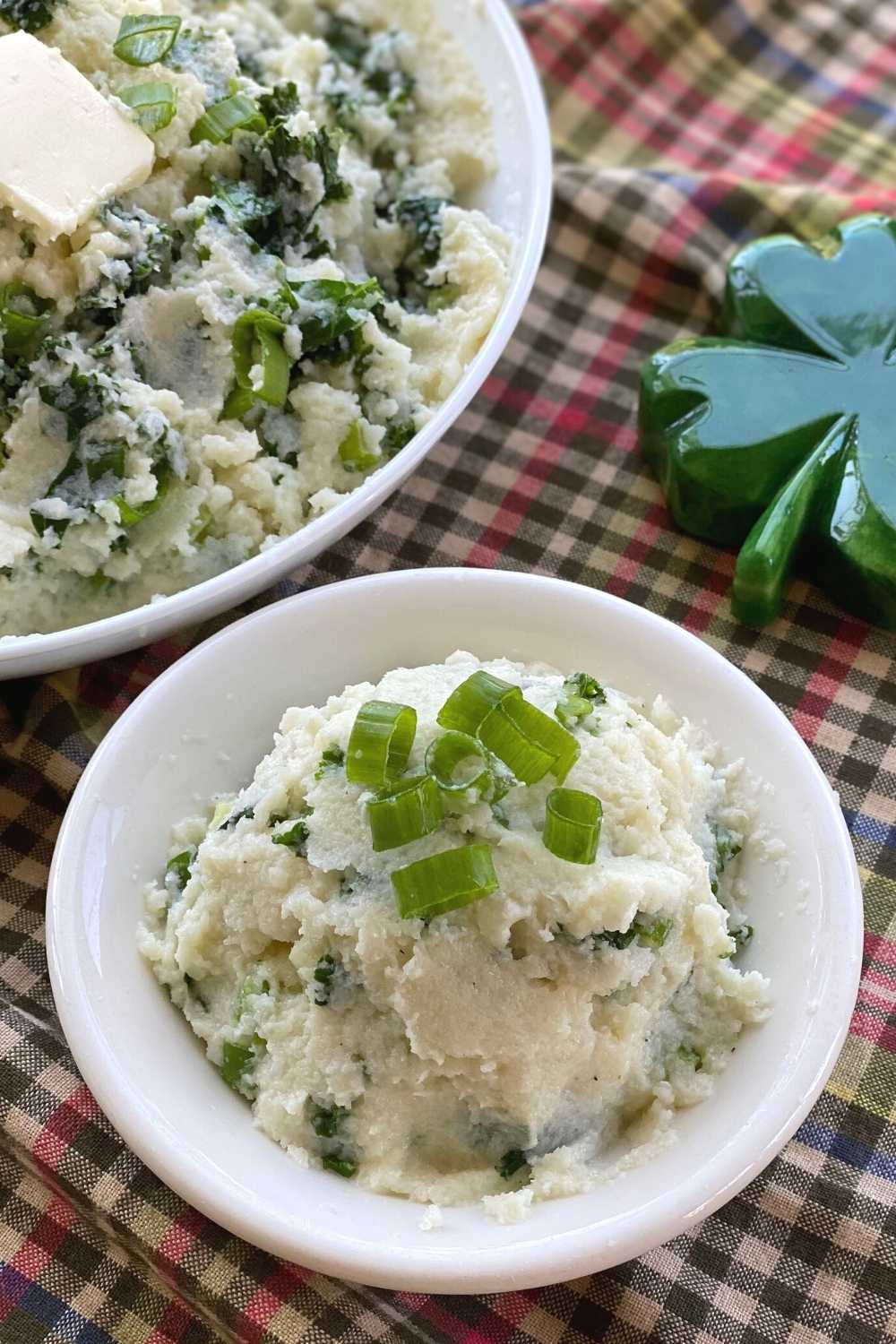 Bowls of Irish mashed cauliflower mixed with kale and green onion next to a shamrock.