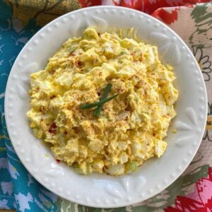 Keto egg salad in bowl next to spoon and lettuce leaves.