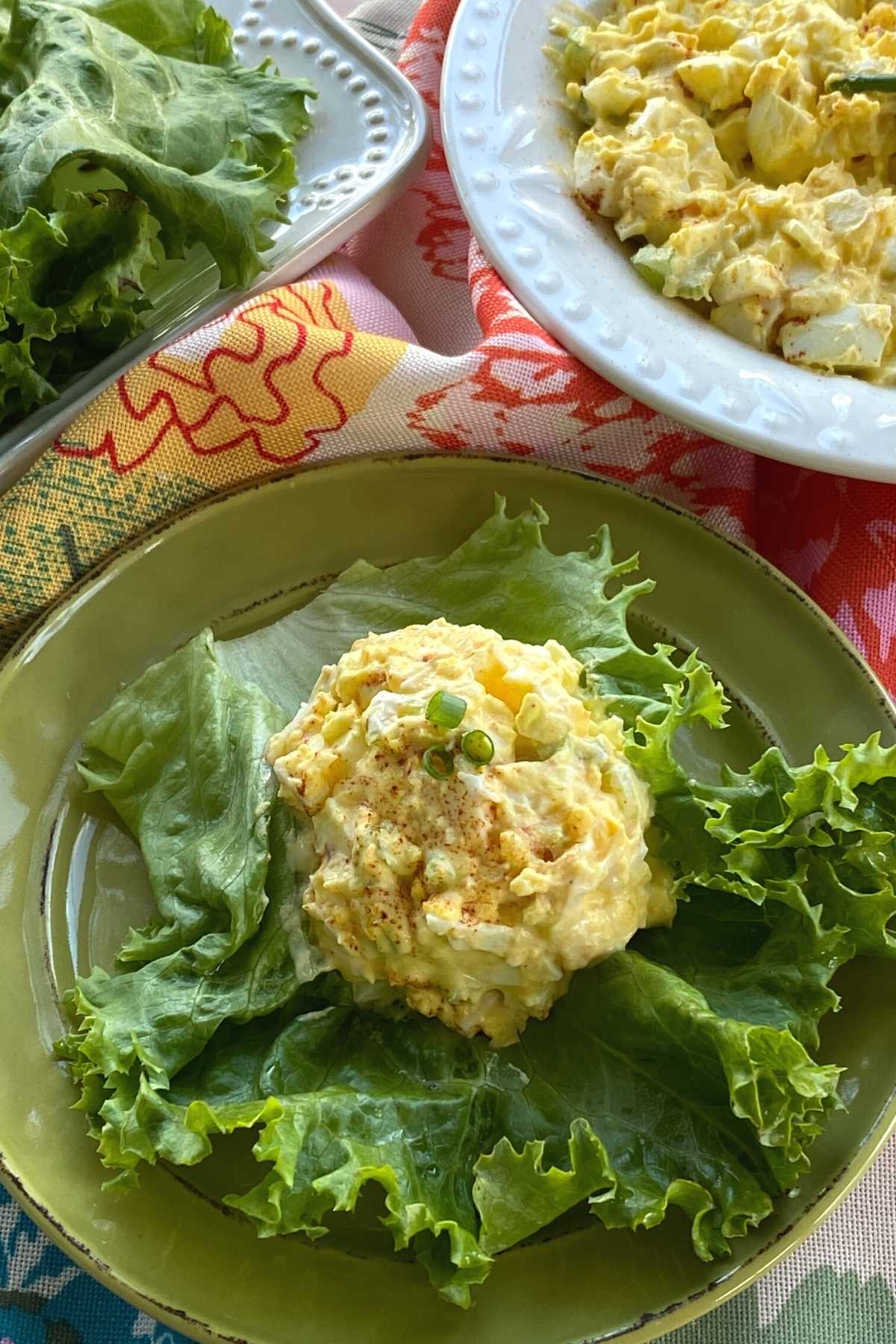 Scoop of low-carb egg salad on a large lettuce leaf with serving bowl and more leaves behind it.