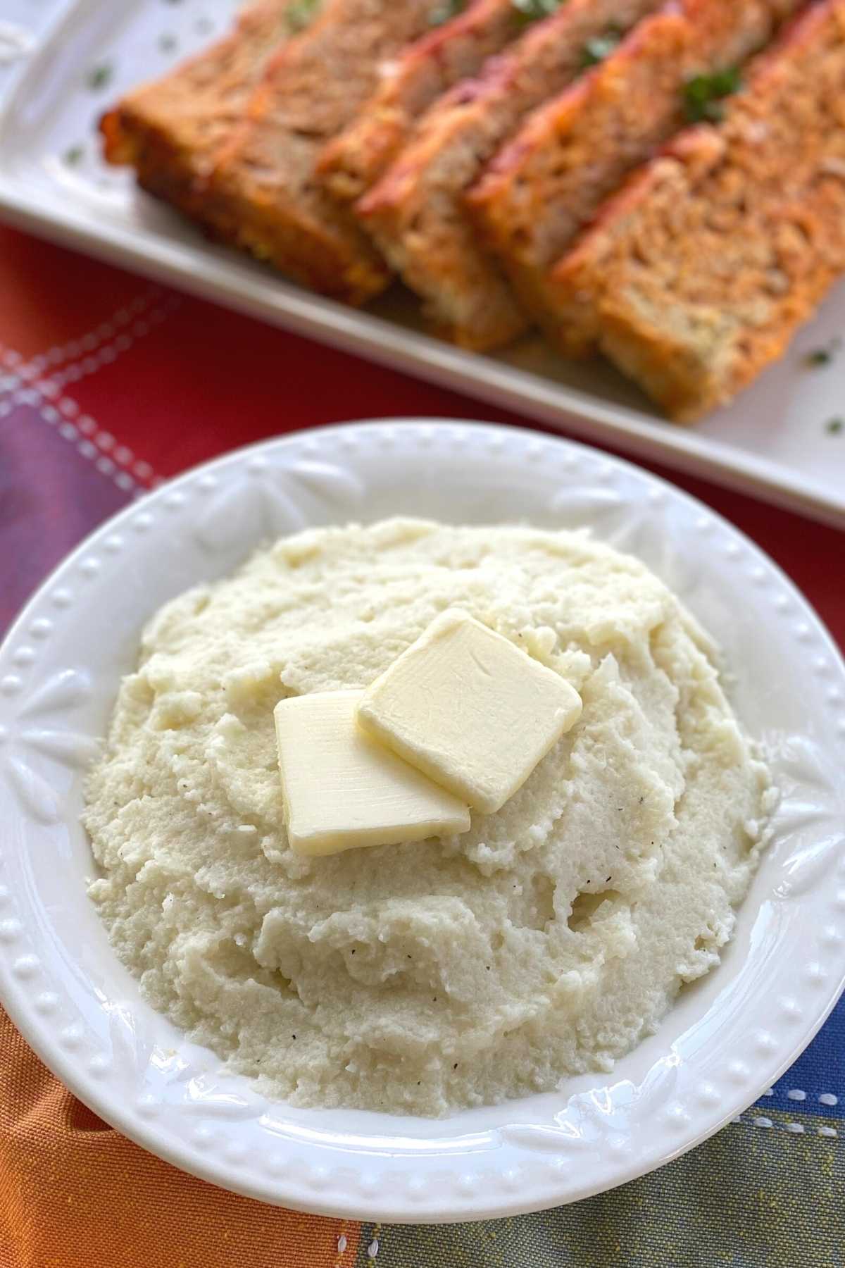 Cauliflower Mashed Potatoes in bowl next to meatloaf on a platter.