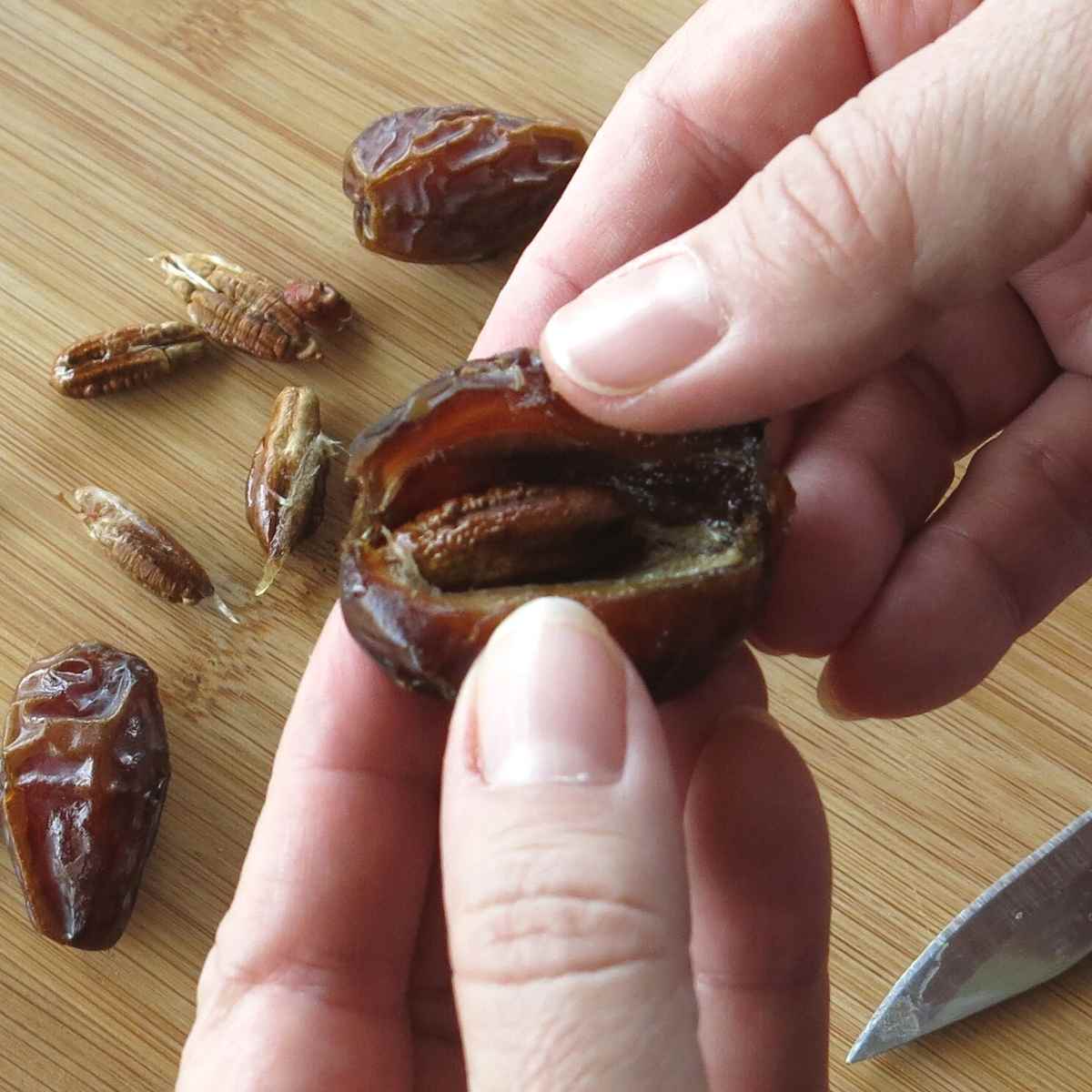 Fingers pulling open a Medjool date to expose the pit.