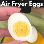 Hand holding half an egg with yolk with air fryer behind it.