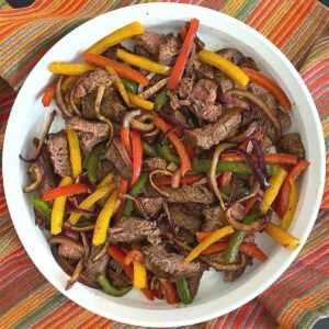 Air fryer steak fajitas with bell peppers and onion in a serving dish.