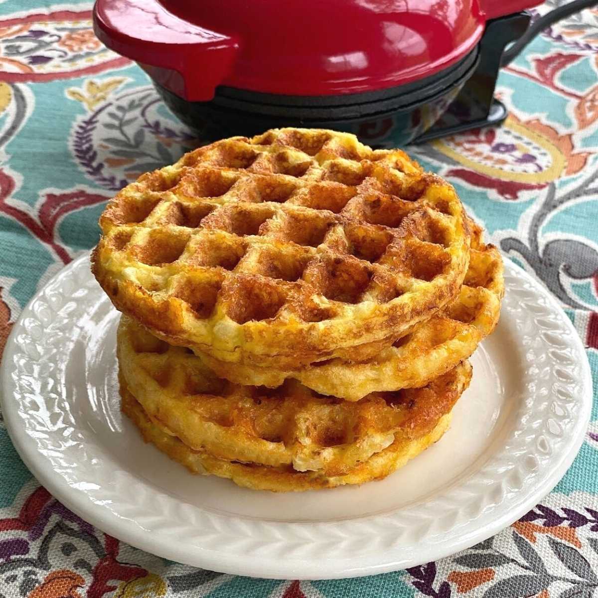 Cauliflower waffles stacked on a plate in front of waffle maker.