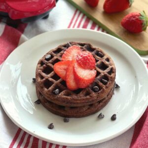 2 Chocolate chaffles on a plate topped with strawberries.