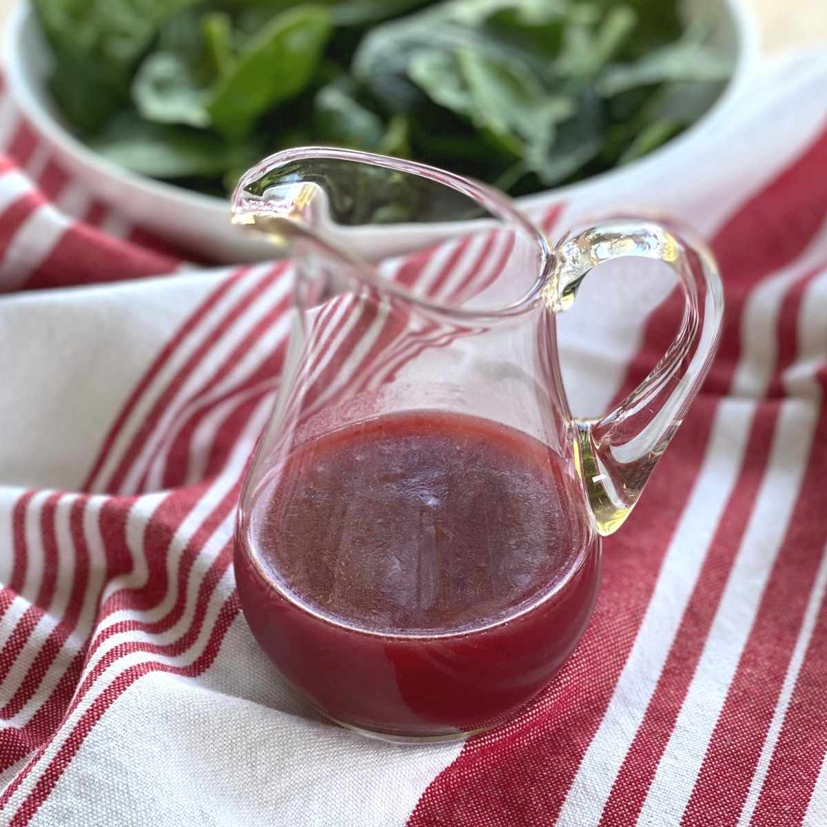 Jam vinaigrette in a pourable container with a bowl of spinach leaves behind it.