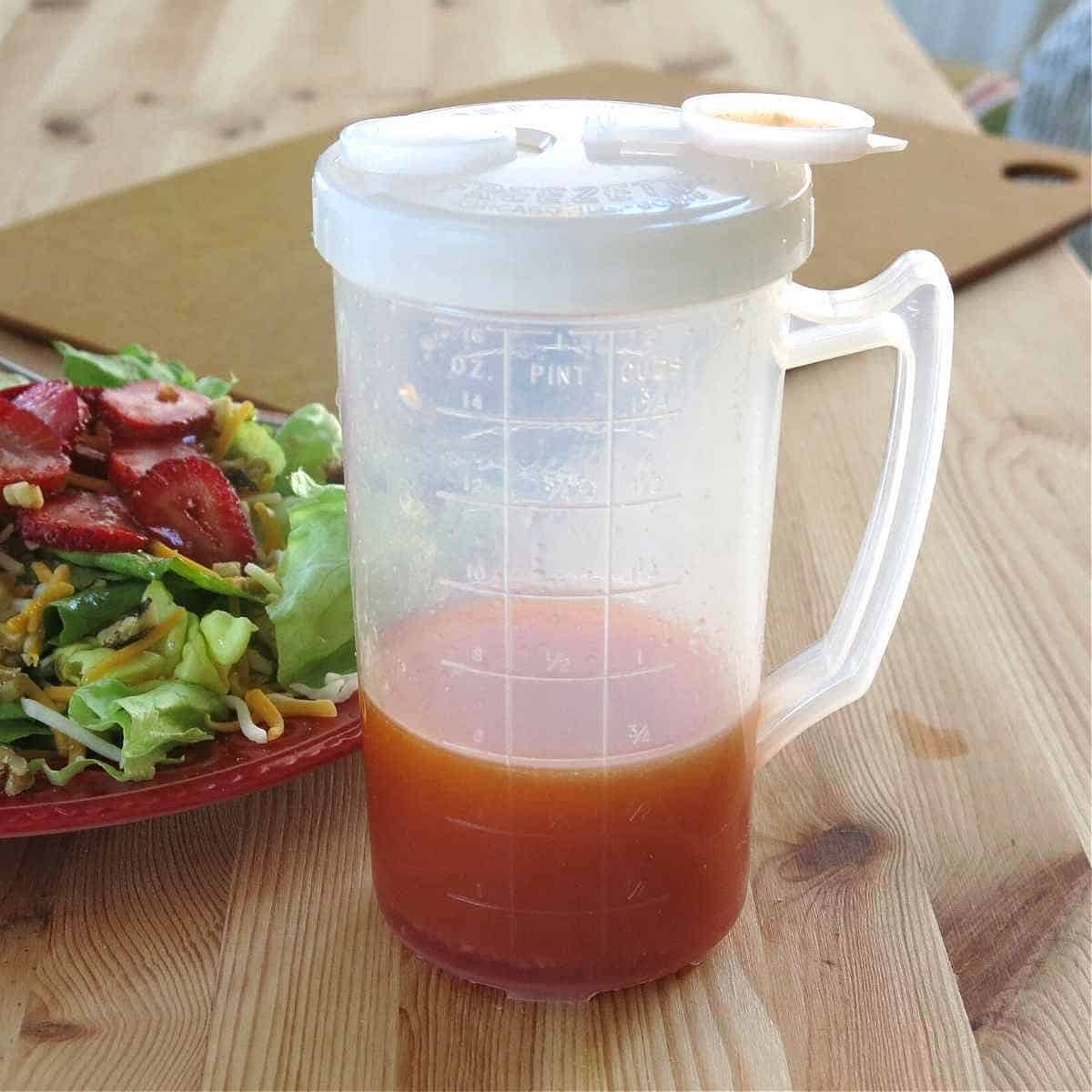 Red wine vinegar dressing in plastic container with measurement markings with strawberry salad next to it.