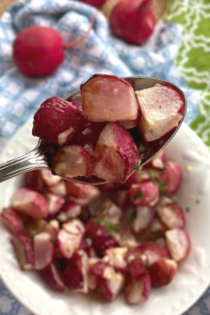 Roasted radishes being lifted out of a bowl on a spoon.