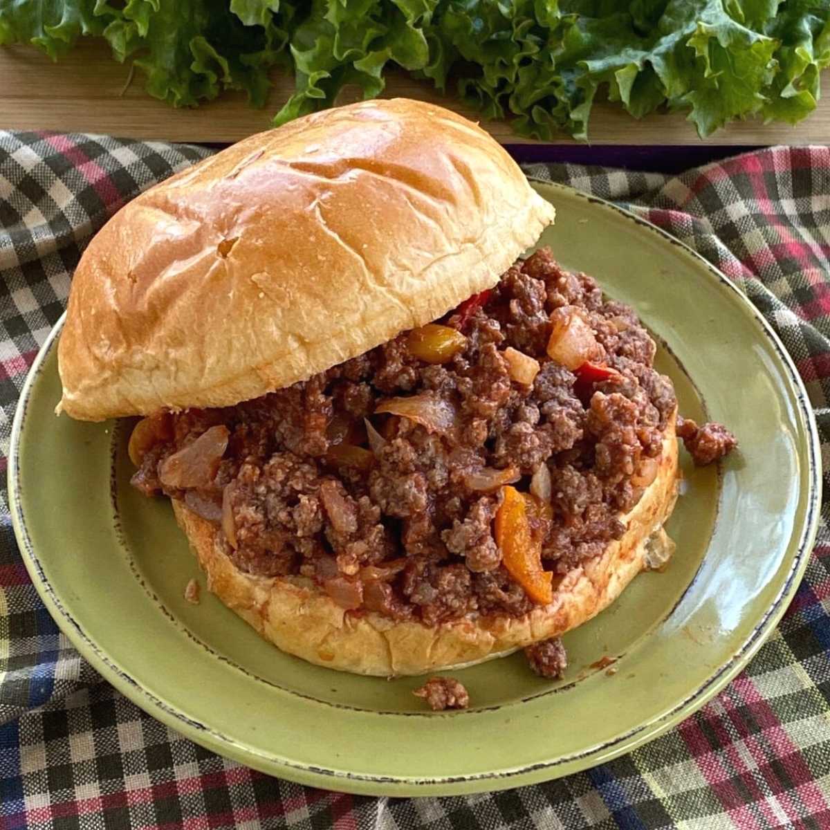 Sloppy Joe on brioche hamburger bun on plate with lettuce leaves behind it.