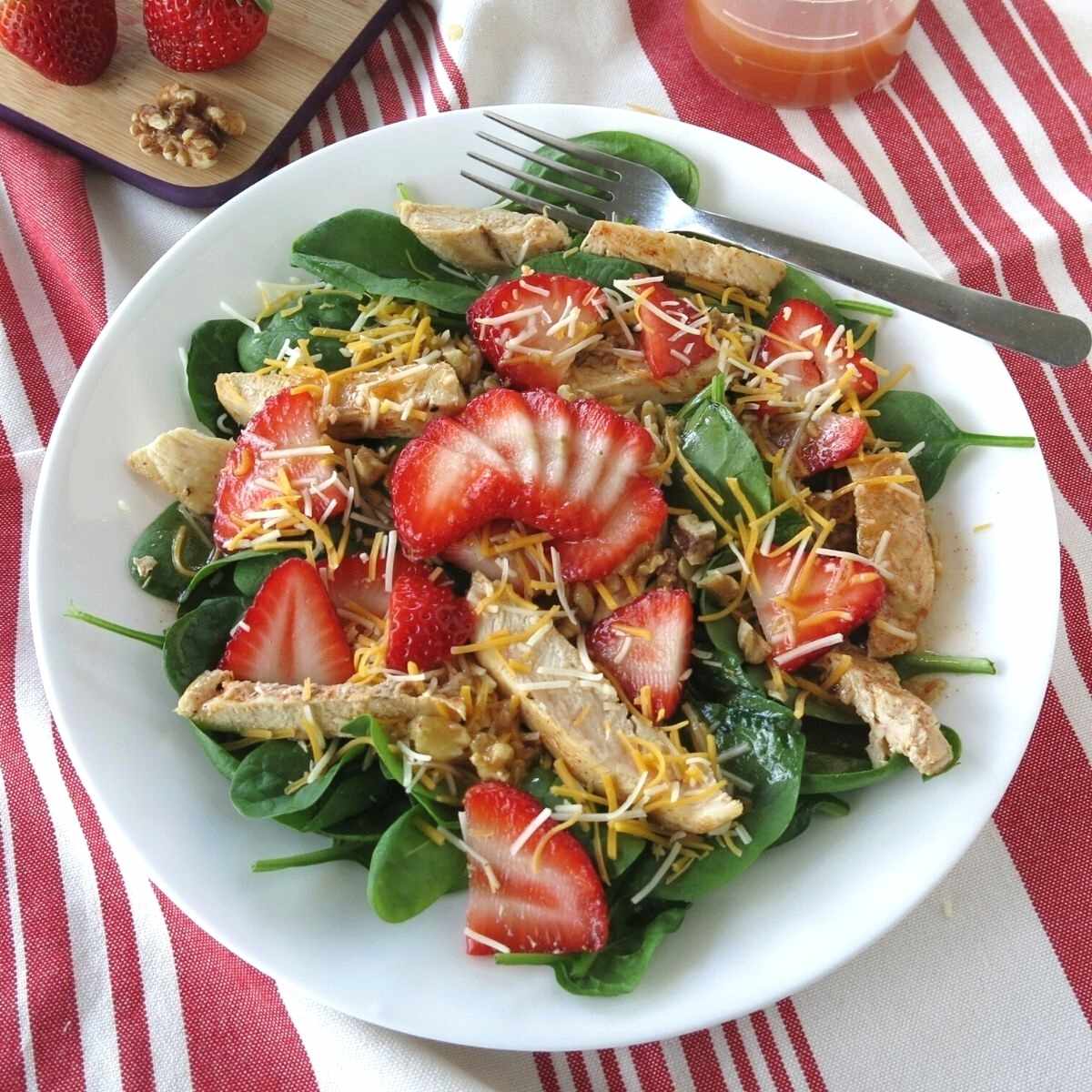 Spinach walnut strawberry salad with cheese and chicken on a plate with a fork.