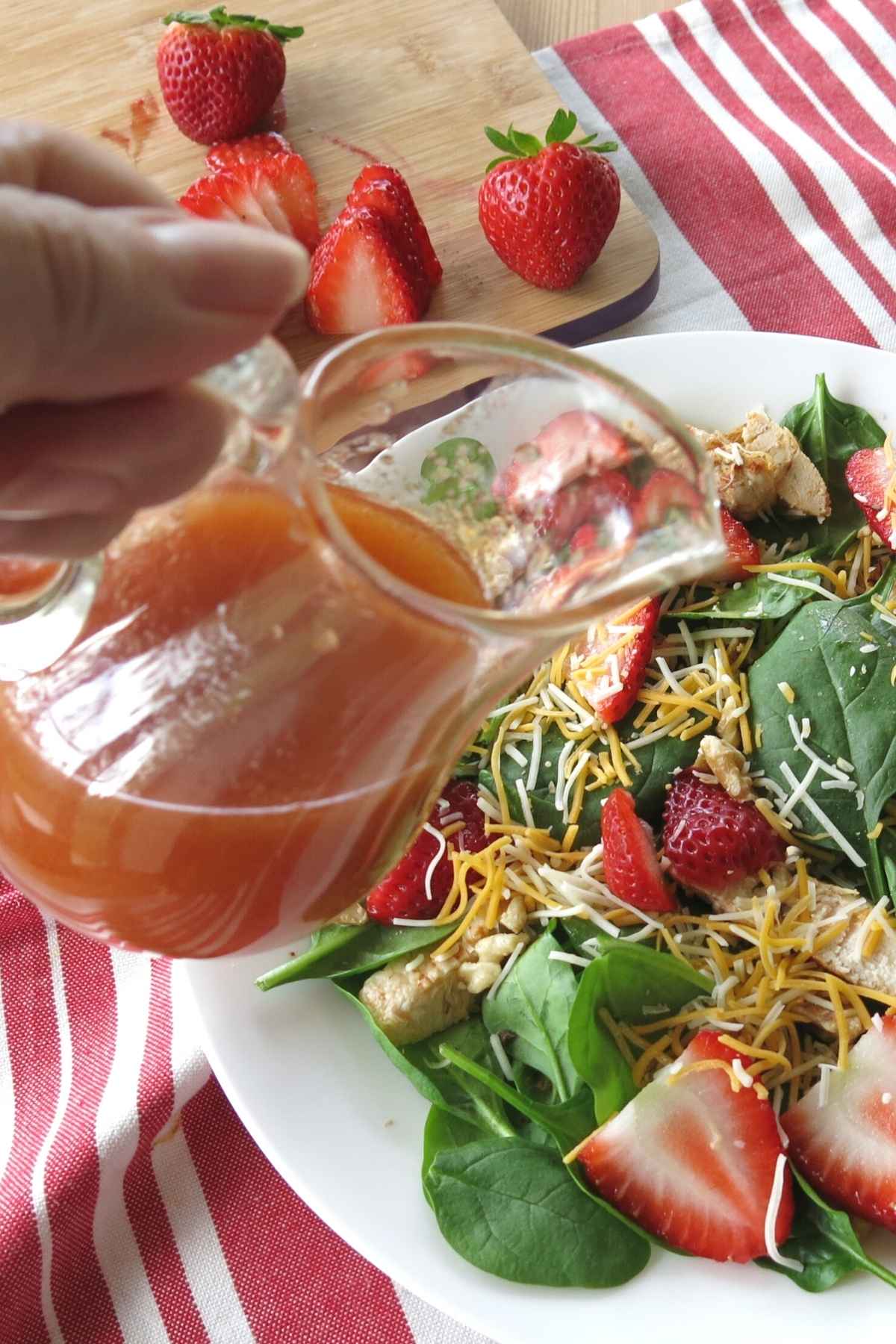 Hand pouring sweet red wine vinaigrette dressing over strawberry salad.