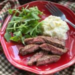 Slices of bavette steak on a plate with mashed cauliflower and arugula.