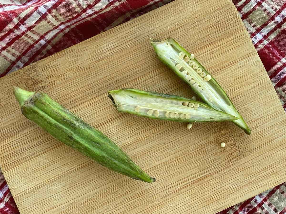 Okra pod cut in half lengthwise next a to a whole fresh pd.