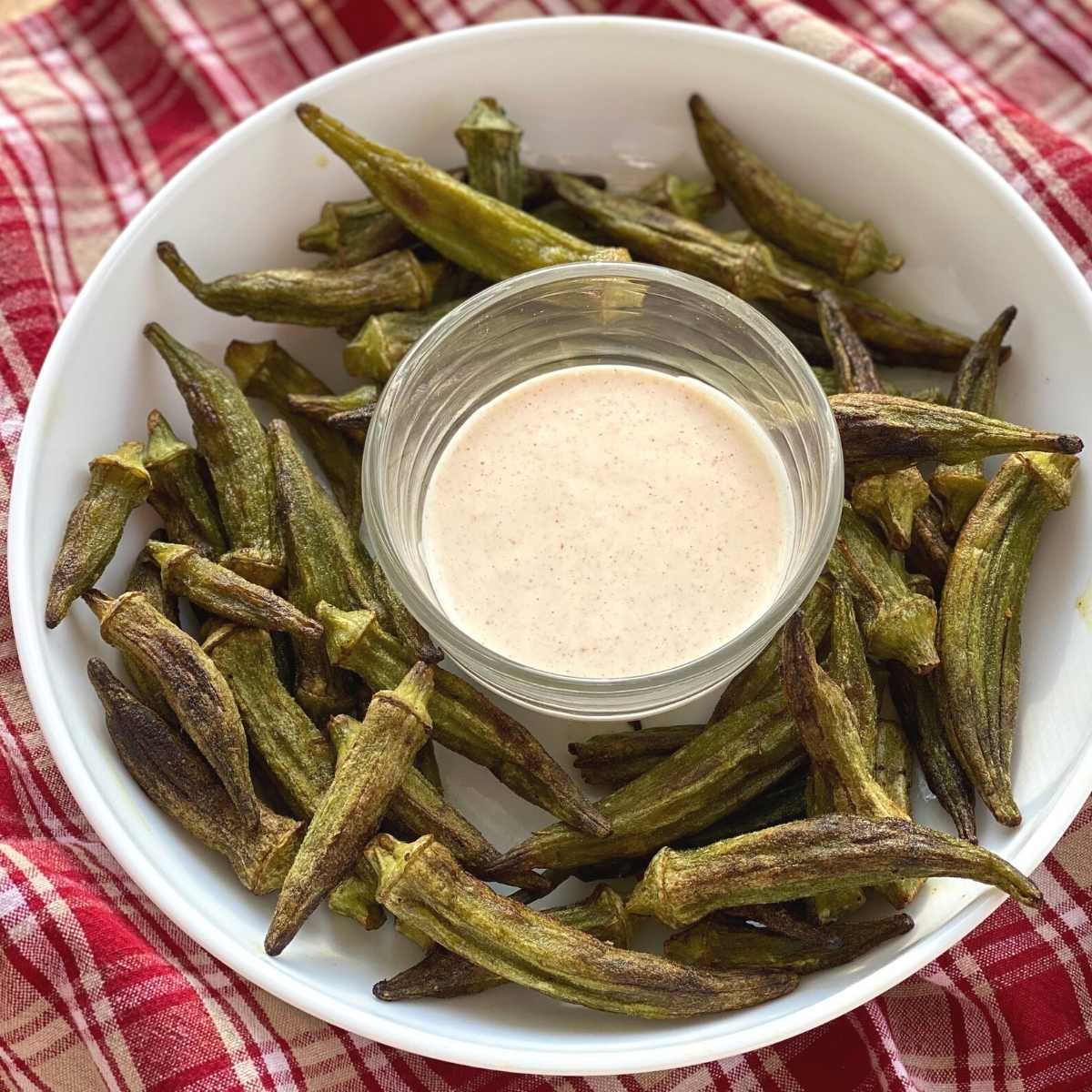 Okra fries on a plate surrounding a bowl of aioli dipping sauce.