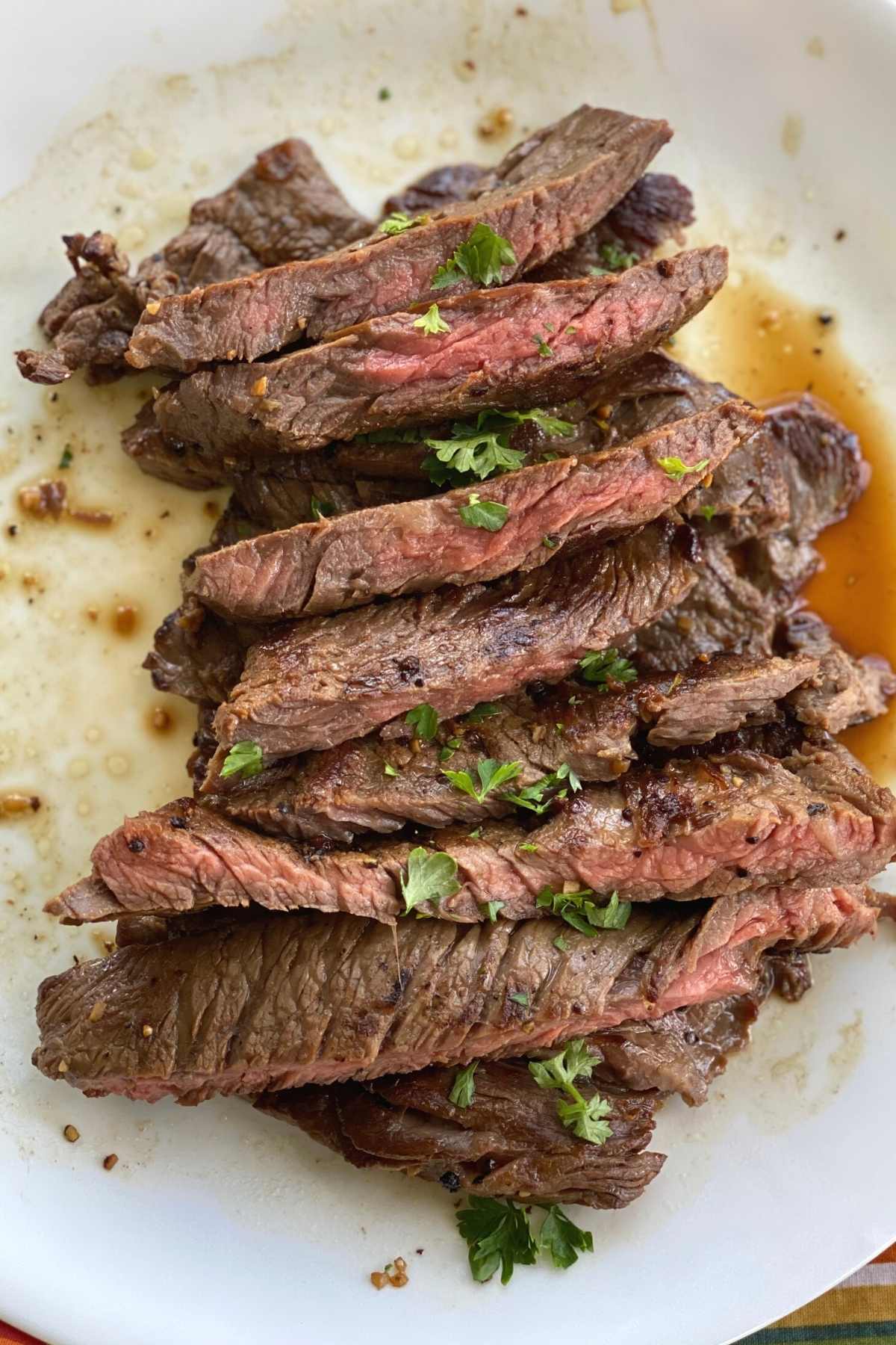 Slices of steak bavette piled on a plate and topped with parsley.