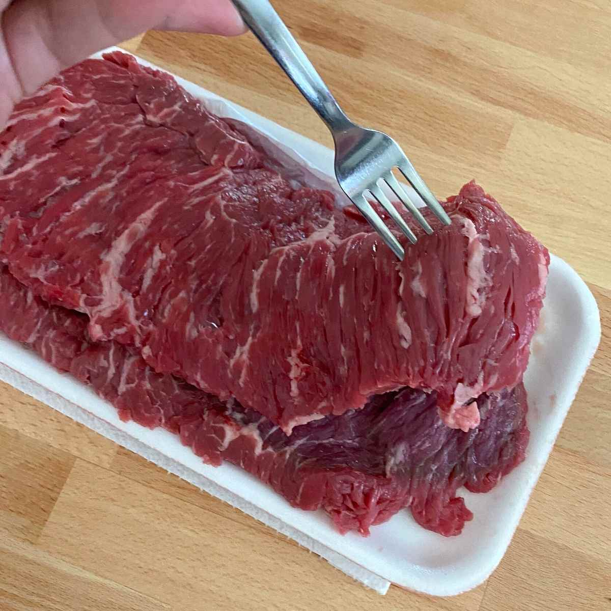 Fork lifting up a uncooked bavette steak to show marbling and loose texture.