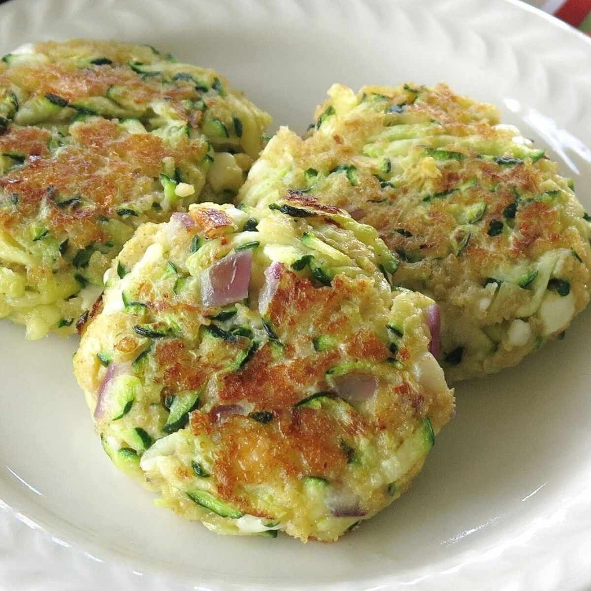 Three fried zucchini cakes with feta cheese on a plate.