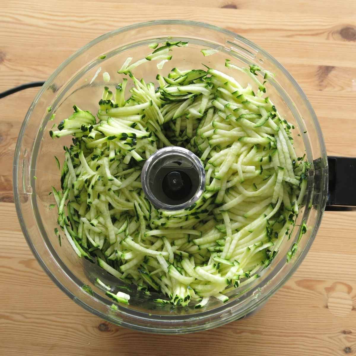 Shredded zucchini in food processor bowl.