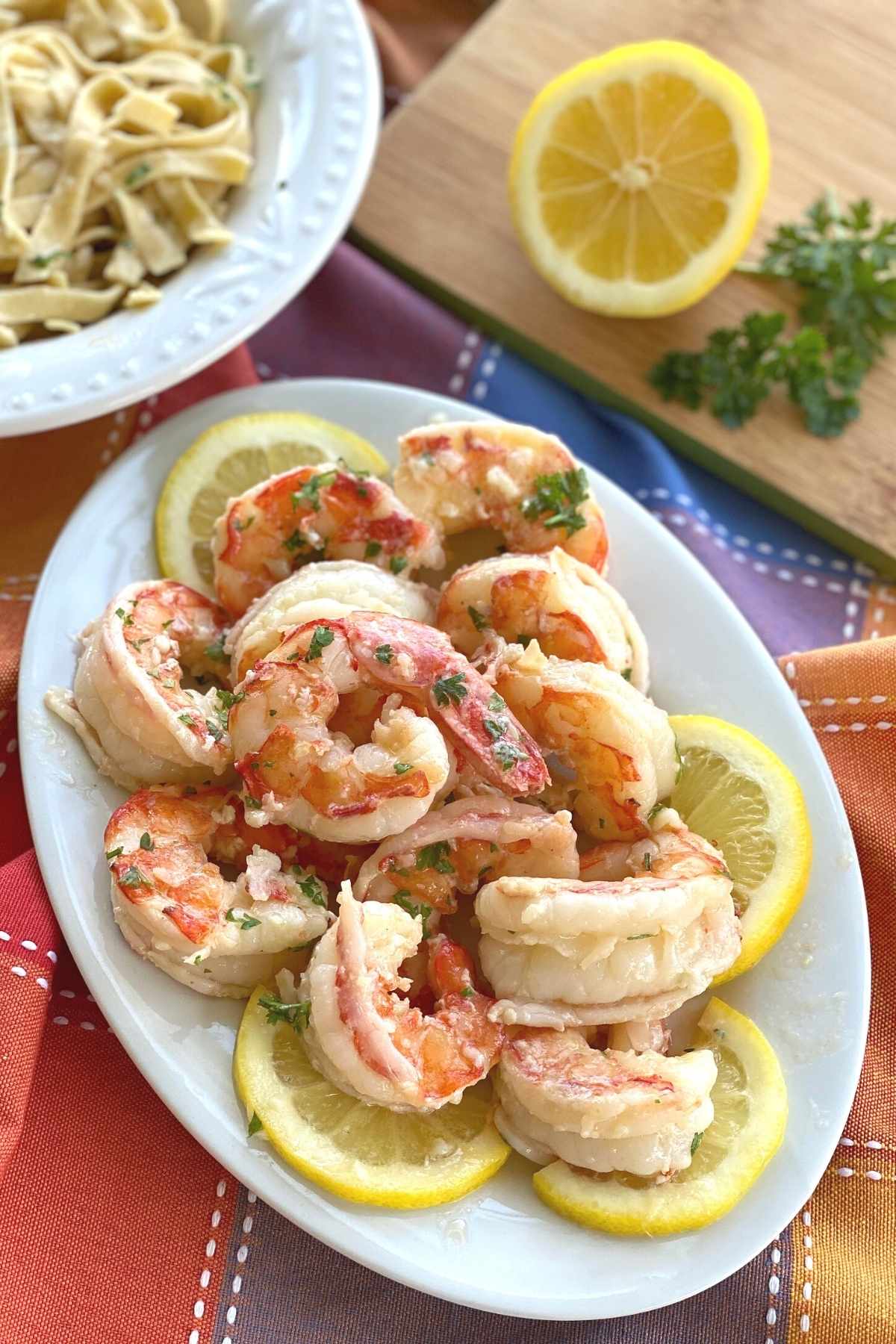 Plate of cooked colossal Argentine red shrimp in a scampi sauce on a plate surrounded by lemon slices.