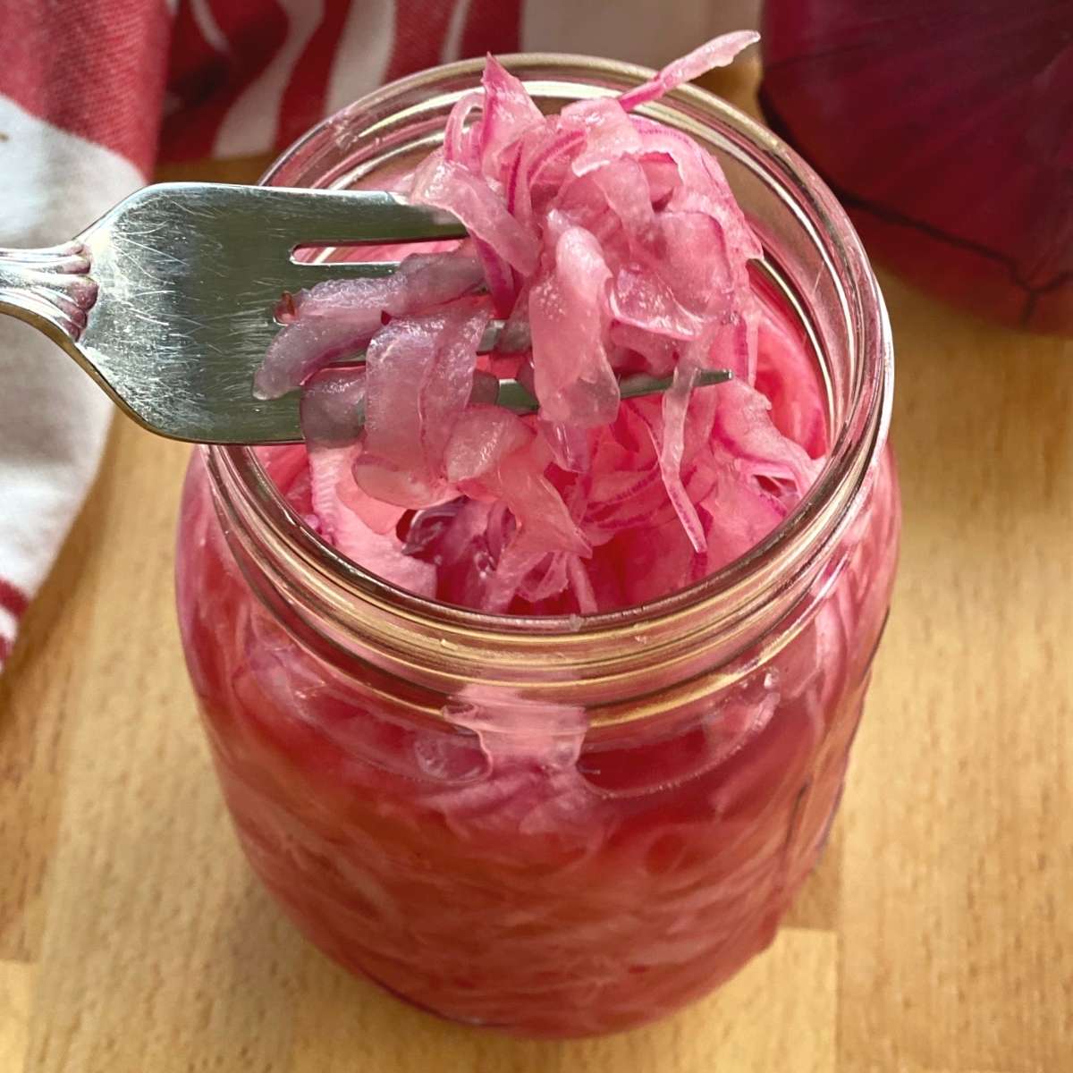 Fork lifting pink pickled onions out of a mason jar.