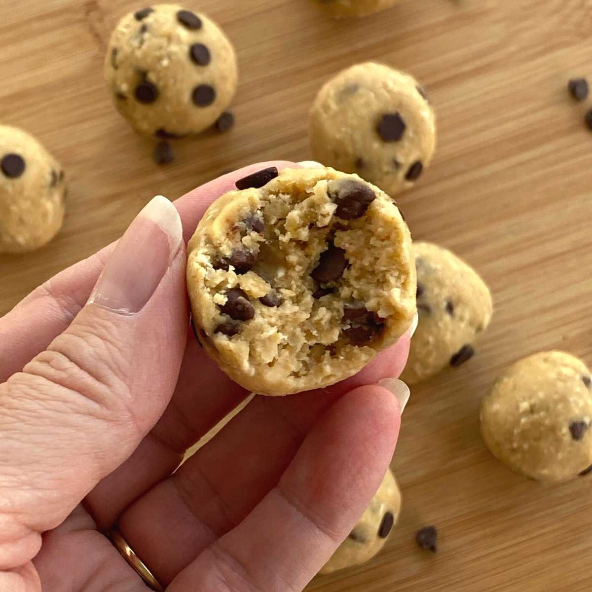 Hand holding chickpea chocolate chip cookie dough ball with a bite taken.