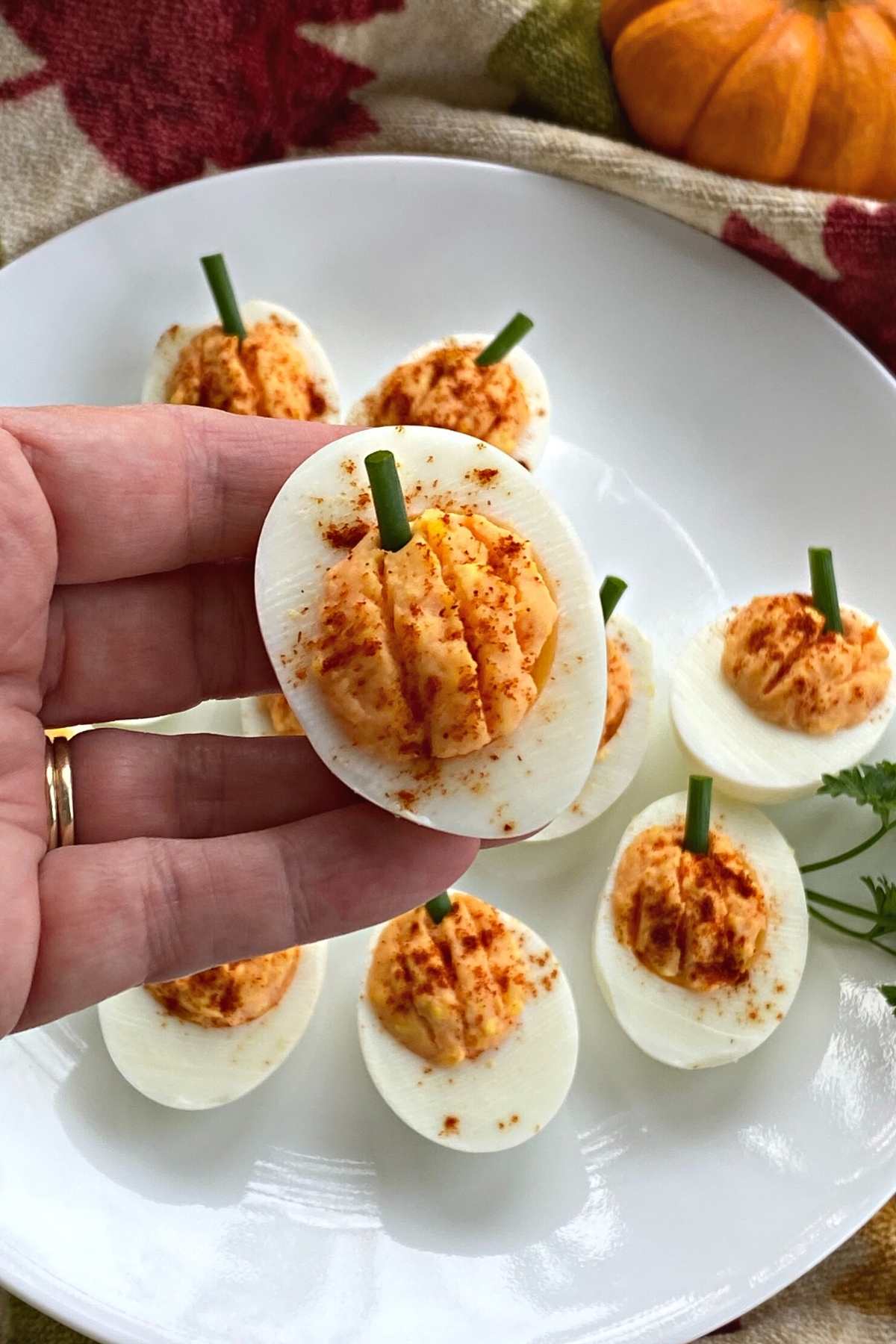 Plate of Halloween pumpkin shaped deviled eggs with hand holding one.